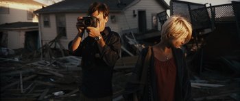 Movie still from “Monsters” (2010), directed by Gareth Edwards – A man taking a picture of a woman with a camera in front of a house; Medium shot, Over the shoulder angle
