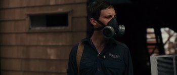 Movie still from “Monsters” (2010), directed by Gareth Edwards – A man wearing a gas mask while standing on a sidewalk; Close Up shot, Over the shoulder angle
