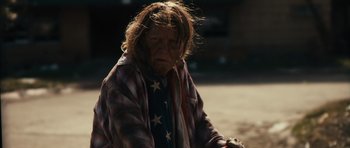 Movie still from “Monsters” (2010), directed by Gareth Edwards – An old woman with a flag on her shirt is sitting on the ground; Medium shot, Over the shoulder angle