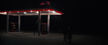 Movie still from “Monsters” (2010), directed by Gareth Edwards – Two people standing in front of a gas station at night; Extreme Wide shot, Low angle