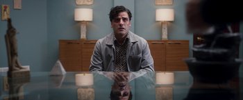 Movie still from “Moon Knight” (2022), directed by Mohamed Diab – A man sitting at a table in front of two lamps; Medium shot, Over the shoulder angle