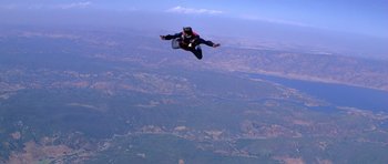 Movie still from “Moonraker” (1979), directed by Lewis Gilbert – A man in black jacket jumping in the air over a field; Extreme Wide shot, High angle