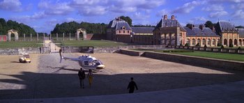Movie still from “Moonraker” (1979), directed by Lewis Gilbert – Two people are standing in front of a helicopter in a field; Extreme Wide shot, High angle