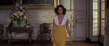 Movie still from “Moonraker” (1979), directed by Lewis Gilbert – A woman in a yellow and white dress in front of a chair; Medium shot, Low angle