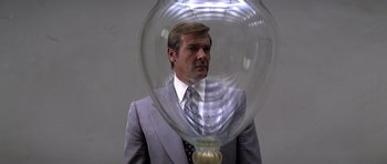 Movie still from “Moonraker” (1979), directed by Lewis Gilbert – A man wearing a suit and tie standing in front of a glass vase; Medium shot, Low angle