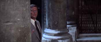 Movie still from “Moonraker” (1979), directed by Lewis Gilbert – A man standing next to a pillar; Medium shot, Over the shoulder angle