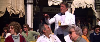 Movie still from “Moonraker” (1979), directed by Lewis Gilbert – A man in a white suit is pouring beer for a man in a black tie; Medium shot, Low angle