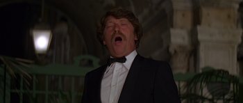 Movie still from “Moonraker” (1979), directed by Lewis Gilbert – A man in a suit and a bow tie is singing; Close Up shot, Low angle