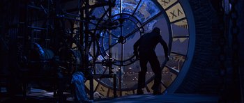 Movie still from “Moonraker” (1979), directed by Lewis Gilbert – A man standing in front of a large clock with a view of the earth; Wide shot, Low angle