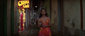 Movie still from “Moonraker” (1979), directed by Lewis Gilbert – A woman in a colorful dress standing in the street; Medium shot, Low angle