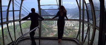 Movie still from “Moonraker” (1979), directed by Lewis Gilbert – A woman in a black dress looking out a window at a city; Wide shot, Low angle