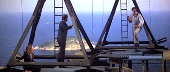 Movie still from “Moonraker” (1979), directed by Lewis Gilbert – A man in a suit standing next to a metal structure; Wide shot, Low angle