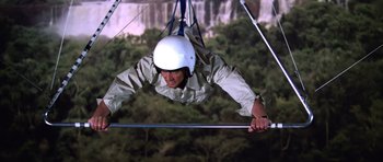 Movie still from “Moonraker” (1979), directed by Lewis Gilbert – A man wearing a white helmet hanging from a bar; Wide shot, Low angle