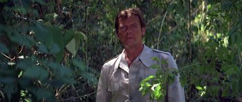 Movie still from “Moonraker” (1979), directed by Lewis Gilbert – A man standing in the middle of a forest looking at the camera; Medium shot, Low angle