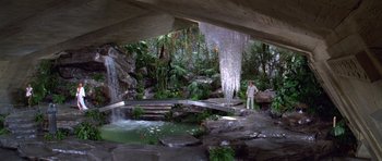 Movie still from “Moonraker” (1979), directed by Lewis Gilbert – A man standing next to a waterfall in a forest; Extreme Wide shot, High angle
