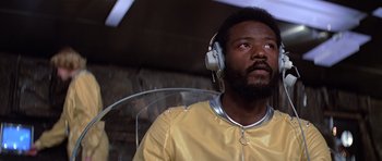 Movie still from “Moonraker” (1979), directed by Lewis Gilbert – A man with a beard wearing headphones and a yellow shirt; Close Up shot, Low angle