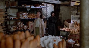 Movie still from “Moonstruck” (1987), directed by Norman Jewison – Two women standing in front of a bakery filled with lots of pastries; Wide shot, Over the shoulder angle