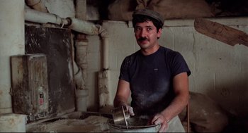 Movie still from “Moonstruck” (1987), directed by Norman Jewison – A man wearing a hat and holding a metal pan; Medium shot, Low angle