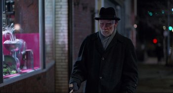 Movie still from “Moonstruck” (1987), directed by Norman Jewison – An older man in a black hat and coat walking down a street; Medium shot, Over the shoulder angle