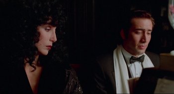 Movie still from “Moonstruck” (1987), directed by Norman Jewison – A man and a woman sitting next to each other in a dark room; Close Up shot, Over the shoulder angle