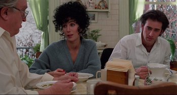 Movie still from “Moonstruck” (1987), directed by Norman Jewison – A woman sitting at a table with a plate of food in front of her; Medium shot, Over the shoulder angle