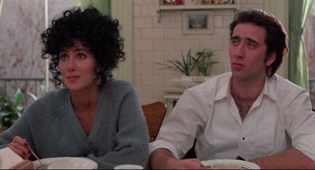 Movie still from “Moonstruck” (1987), directed by Norman Jewison – A man and a woman sitting next to each other at a table; Medium shot, Over the shoulder angle