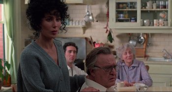 Movie still from “Moonstruck” (1987), directed by Norman Jewison – A group of people sitting around a table in a room; Medium shot, Over the shoulder angle