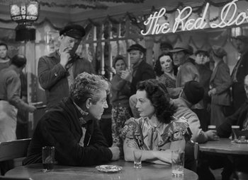Movie still from “Moontide” (1942), directed by Fritz Lang – A man and a woman sitting at a table in front of a crowd; Medium shot, High angle