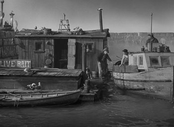 Movie still from “Moontide” (1942), directed by Fritz Lang – Two men standing on a dock next to a house; Wide shot, High angle