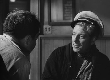 Movie still from “Moontide” (1942), directed by Fritz Lang – A man wearing a hat talking to another man in front of a building; Medium shot, Over the shoulder angle