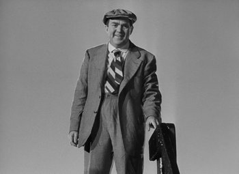 Movie still from “Moontide” (1942), directed by Fritz Lang – A man in a suit and hat holding a guitar case; Medium shot, Low angle