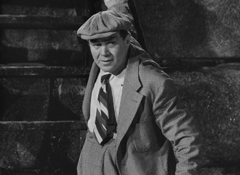 Movie still from “Moontide” (1942), directed by Fritz Lang – A man in a suit and hat is standing outside; Medium shot, Low angle