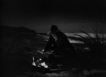 Movie still from “Moontide” (1942), directed by Fritz Lang – A man in a cowboy hat sitting on the ground near a fire; Wide shot, High angle