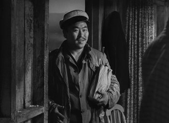 Movie still from “Moontide” (1942), directed by Fritz Lang – A man in a hat standing next to a window; Medium shot, Low angle