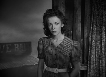 Movie still from “Moontide” (1942), directed by Fritz Lang – A woman wearing a plaid dress with a belt around her waist; Medium shot, Low angle