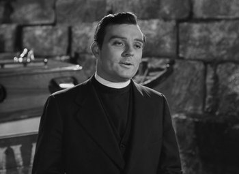 Movie still from “Moontide” (1942), directed by Fritz Lang – A man in a priest's outfit standing in front of a stone wall; Medium shot, Low angle