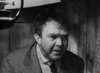 Movie still from “Moontide” (1942), directed by Fritz Lang – Black and white photograph of a man wearing a suit and tie; Close Up shot, Low angle