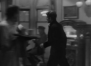 Movie still from “Moontide” (1942), directed by Fritz Lang – A black and white photo of a man in a suit walking; Medium shot, Over the shoulder angle