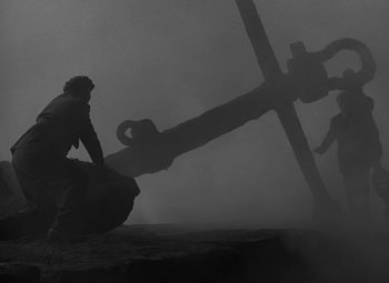 Movie still from “Moontide” (1942), directed by Fritz Lang – A man sitting on top of a rock next to an anchor; Extreme Wide shot, High angle