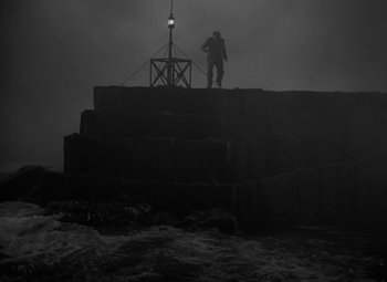 Movie still from “Moontide” (1942), directed by Fritz Lang – A man standing on top of a pile of rocks near the ocean; Extreme Wide shot, High angle