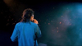 Movie still from “Moonwalker” (1988), directed by Jerry Kramer – A man standing in front of a stage with lights; Extreme Wide shot, High angle