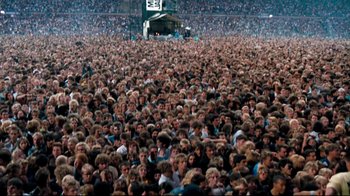 Movie still from “Moonwalker” (1988), directed by Jerry Kramer – A crowd of people sitting in a stadium; Extreme Wide shot, High angle