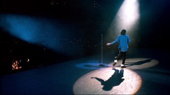 Movie still from “Moonwalker” (1988), directed by Jerry Kramer – A man standing on a stage in front of a microphone; Wide shot, High angle