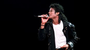 Movie still from “Moonwalker” (1988), directed by Jerry Kramer – A man in a black jacket is singing into a microphone; Medium shot, Low angle