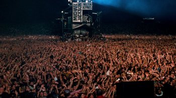 Movie still from “Moonwalker” (1988), directed by Jerry Kramer – A crowd of people at an event in front of a stage; Extreme Wide shot, High angle