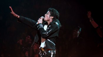 Movie still from “Moonwalker” (1988), directed by Jerry Kramer – A man is singing into a microphone on a stage; Medium shot, Low angle