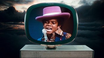 Movie still from “Moonwalker” (1988), directed by Jerry Kramer – A television screen with a picture of a young boy singing; Close Up shot, Low angle