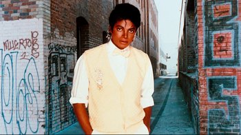 Movie still from “Moonwalker” (1988), directed by Jerry Kramer – A man in a vest and bow tie standing on a sidewalk; Medium shot, Low angle