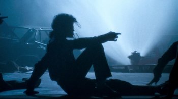Movie still from “Moonwalker” (1988), directed by Jerry Kramer – A person sitting on the ground in the dark; Wide shot, Low angle