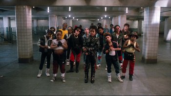 Movie still from “Moonwalker” (1988), directed by Jerry Kramer – A group of young people standing around each other in a hallway; Wide shot, Overhead angle